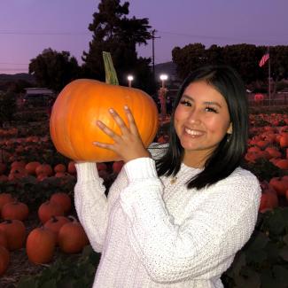 monica holding a pumpkin in front of a pumpkin patch